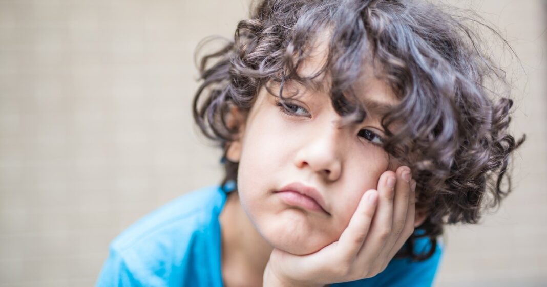 Niño pensativo mirando por la ventana, representando un momento de aburrimiento e introspección.