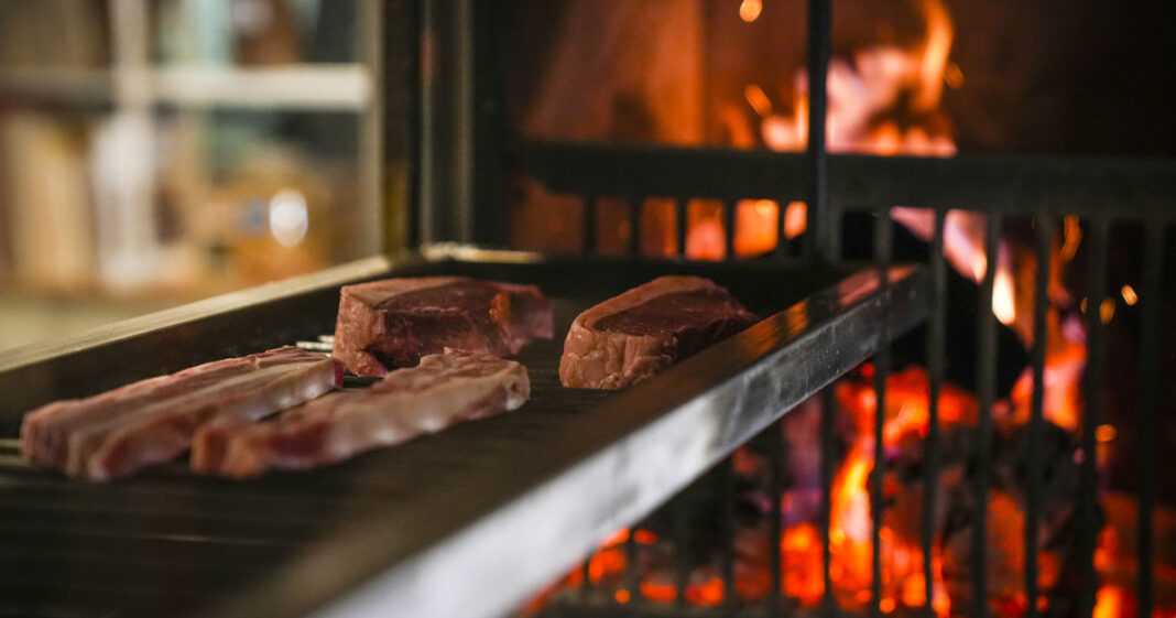Persona frotando un diente de ajo sobre los hierros de una parrilla caliente.