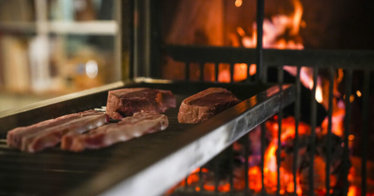 Persona frotando un diente de ajo sobre los hierros de una parrilla caliente.