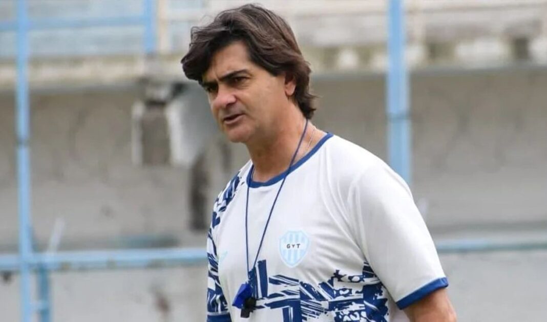 Rubén Forestello, entrenador de fútbol argentino, junto al escudo de Estudiantes de Río Cuarto