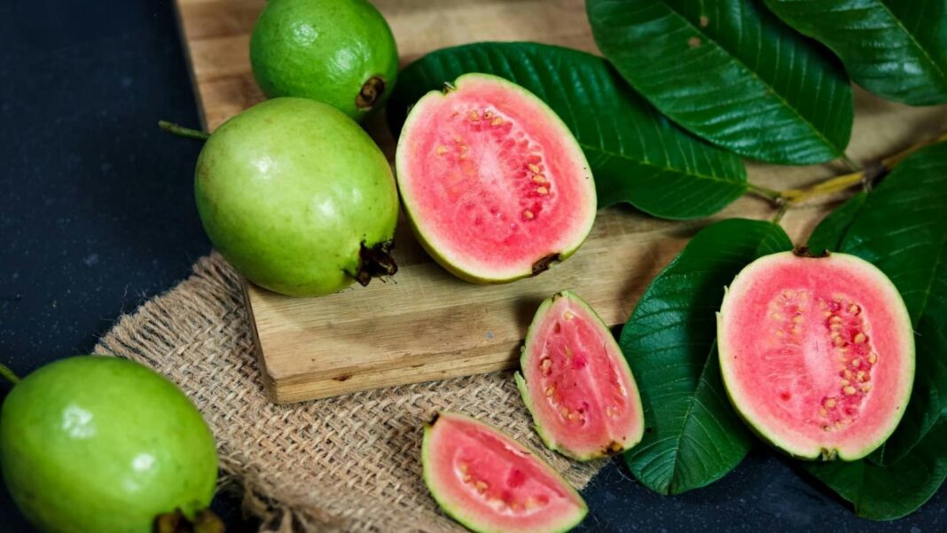 Zumo de guayaba en un vaso junto a guayabas frescas