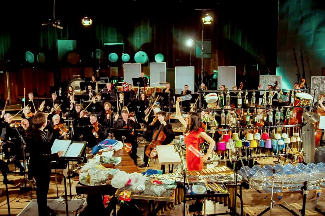 Fotografía de una orquesta sinfónica con percusionista tocando instrumentos hechos con residuos