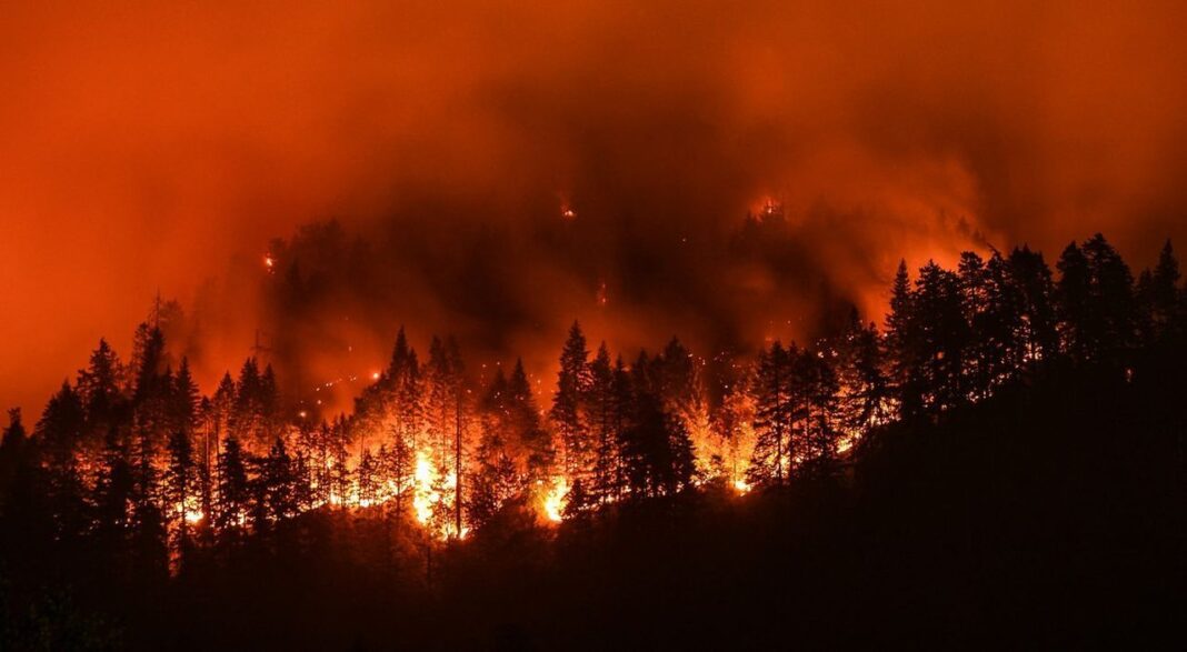 Incendio forestal en California con columna de humo y helicóptero hidrante