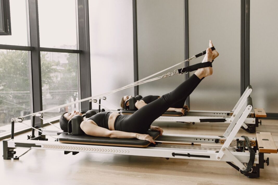 Instructora de pilates junto a una cama reformer en un centro de entrenamiento